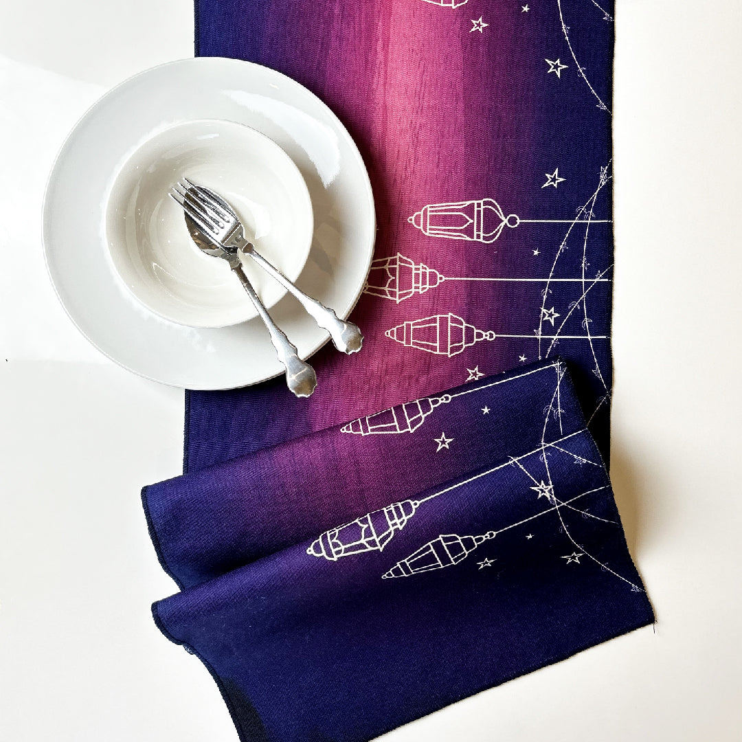 white tableware on a folded purple table runner with white lanterns print